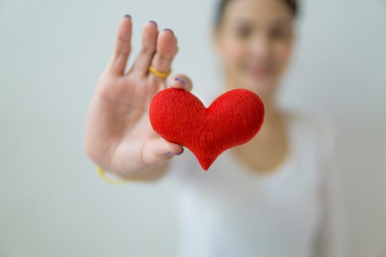 Close-up of a woman holding a red heart symbolizing love, care, and health.